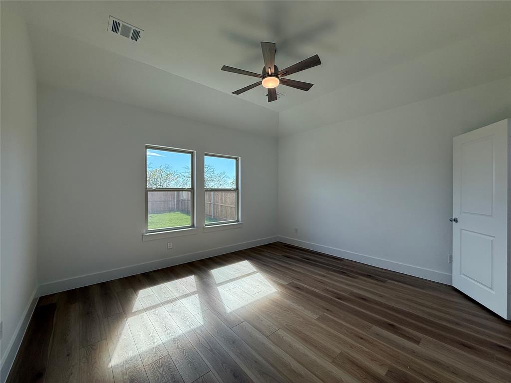 Room featuring wood-finish flooring, tray ceiling, central ceiling fan with integrated lighting, and dual windows