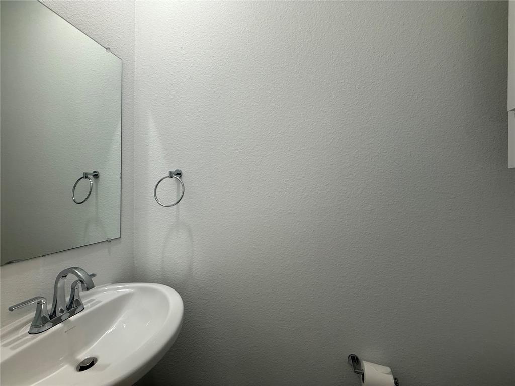 Wall-mounted frameless mirror, pedestal sink with a dual-handle chrome faucet, and circular metal towel ring