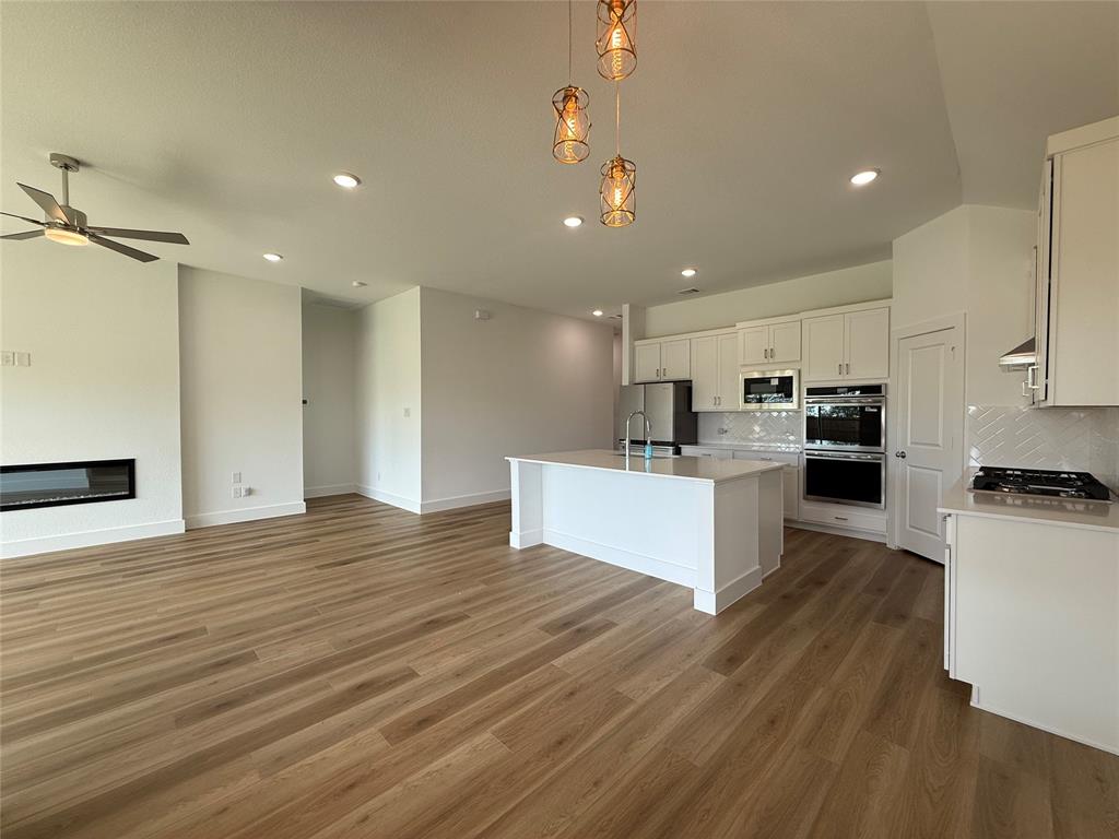 Open-concept living space featuring wood-finish flooring, a linear electric fireplace, a kitchen island, recessed lighting, and built-in stainless steel double ovens