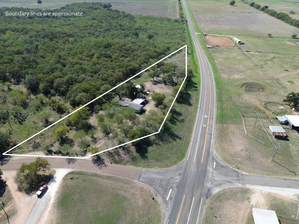 Aerial perspective of a corner lot featuring mature trees, wooded acreage, and paved road access