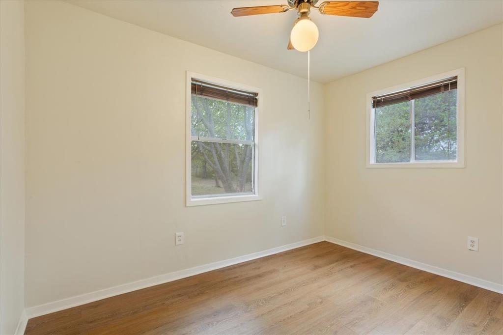 Neutral-toned room featuring wood-finish flooring, two sliding windows, and a ceiling fan with integrated lighting
