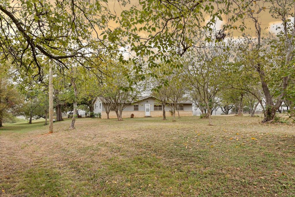 Expansive lot featuring mature trees and a single-story residence with light-toned horizontal siding and stone masonry exterior