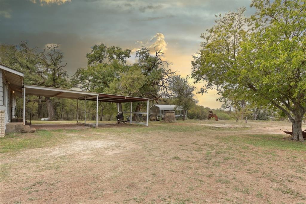 Expansive acreage featuring mature trees, a metal-roofed carport, and a secondary metal storage structure
