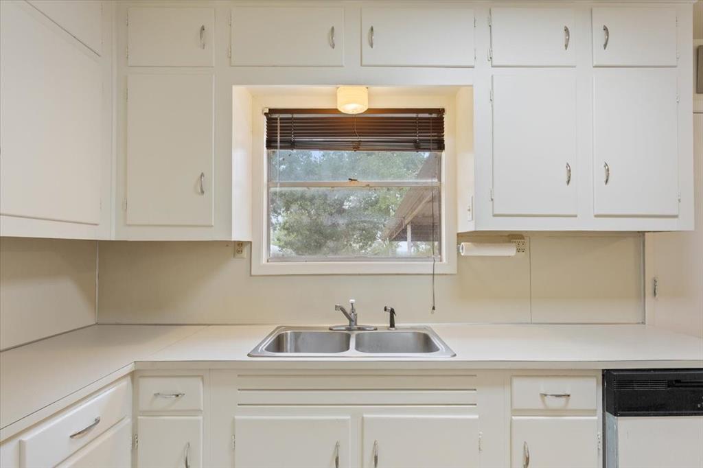 Kitchen featuring white cabinetry, solid-surface countertops, dual-basin stainless steel sink with pull-out sprayer faucet, and natural light via a central window