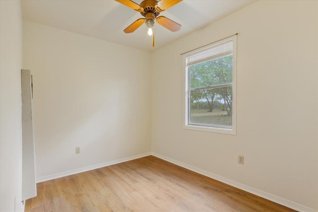 Interior room featuring wood-finish flooring, a ceiling fan with integrated lighting, and a window with wood-frame trim