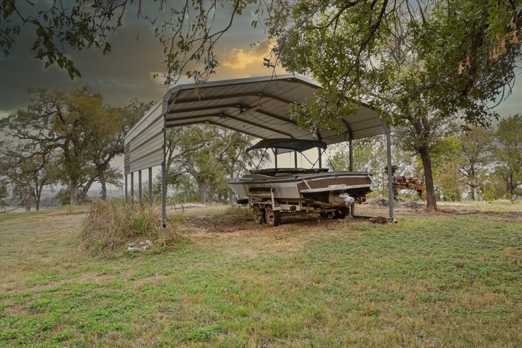 Freestanding metal carport structure with a gabled roof, supported by steel posts on a grass-covered lot featuring mature trees