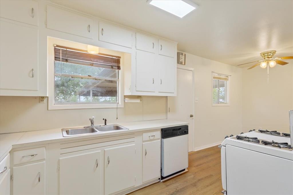 Kitchen featuring white cabinetry with overhead storage, a double-basin stainless steel sink, wood-finish flooring, and a ceiling-mounted light fixture