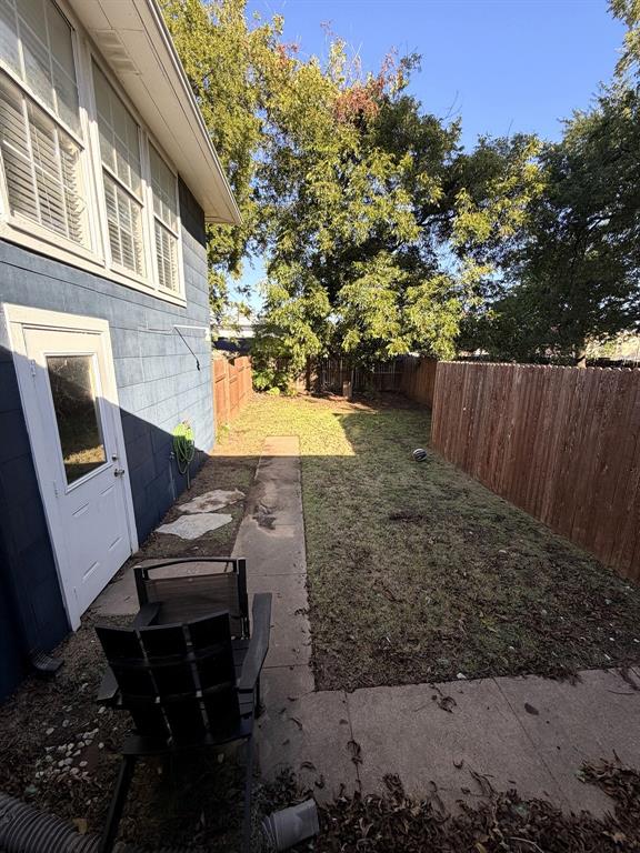 Private backyard featuring a grass lawn, perimeter wood fencing, concrete walkway, and mature trees