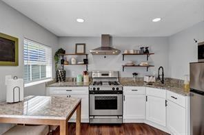 Kitchen featuring white shaker-style cabinetry, stone-surface countertops, stainless steel range with a professional-style vent hood, open shelving, and wood-finish flooring