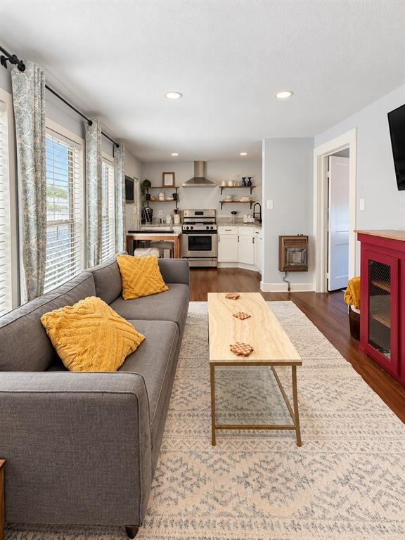 Open-concept floor plan featuring wood-finish flooring, stainless steel range with overhead chimney hood, white cabinetry, and recessed lighting