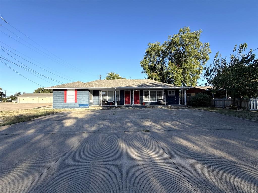 Single-story exterior featuring blue siding, red accent shutters, two separate entry doors, a wide concrete driveway, and a covered front porch