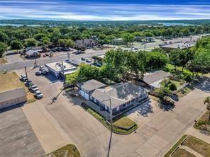 Aerial perspective of a single-story structure with a multi-gabled roof, featuring an attached garage, extensive paved parking area, and mature landscaping