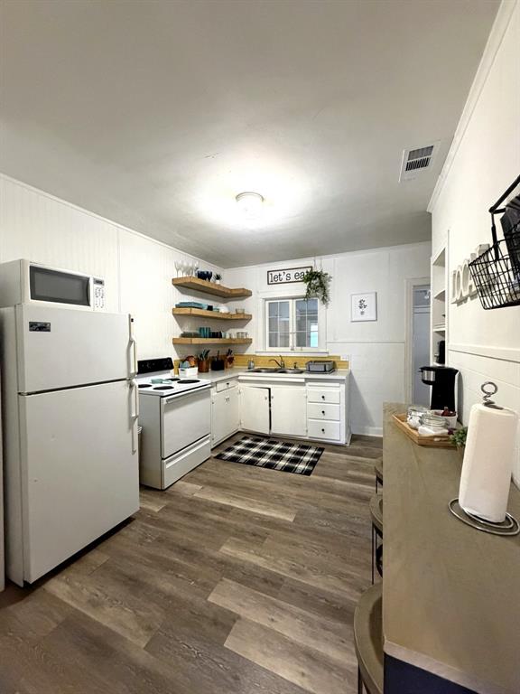 Kitchen featuring wood-finish flooring, white cabinetry, open wooden shelving, and a dual-basin sink with a window backsplash