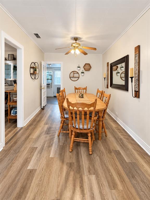 Dining area featuring wood-finish flooring, crown molding, and a central ceiling fan with integrated lighting