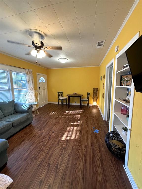Living space featuring wood-finish flooring, built-in shelving, a ceiling fan with integrated lighting, and a multi-pane glass entry door