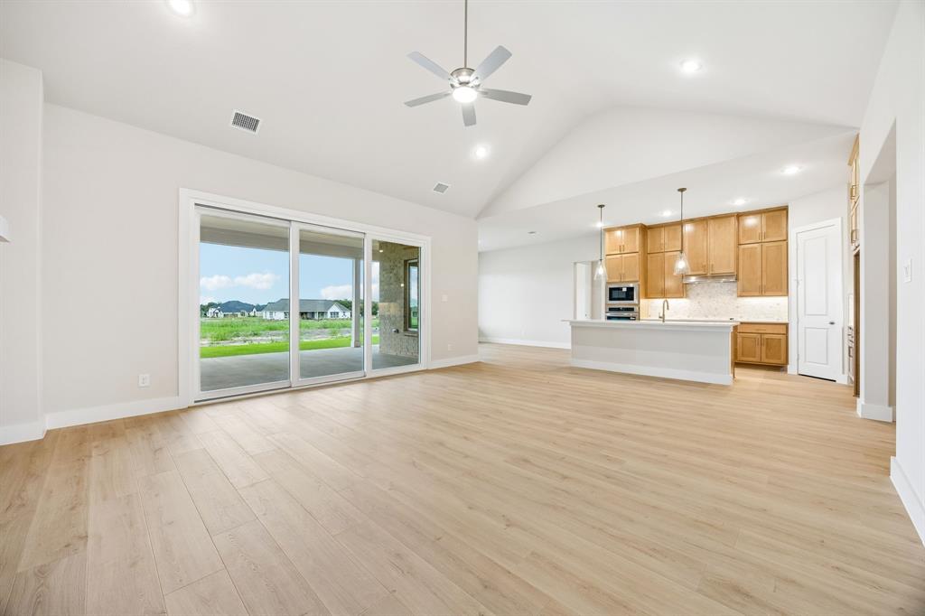 Open-concept interior featuring vaulted ceilings, wood-finish flooring, sliding glass doors, a kitchen island, and built-in cabinetry
