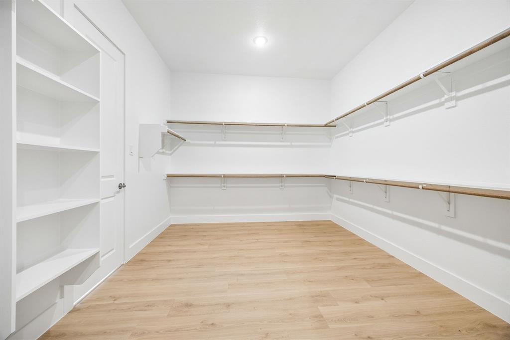 Walk-in closet featuring wood-finish flooring, built-in shelving unit, dual-level wall-mounted shelving with integrated hanging rods, and recessed lighting