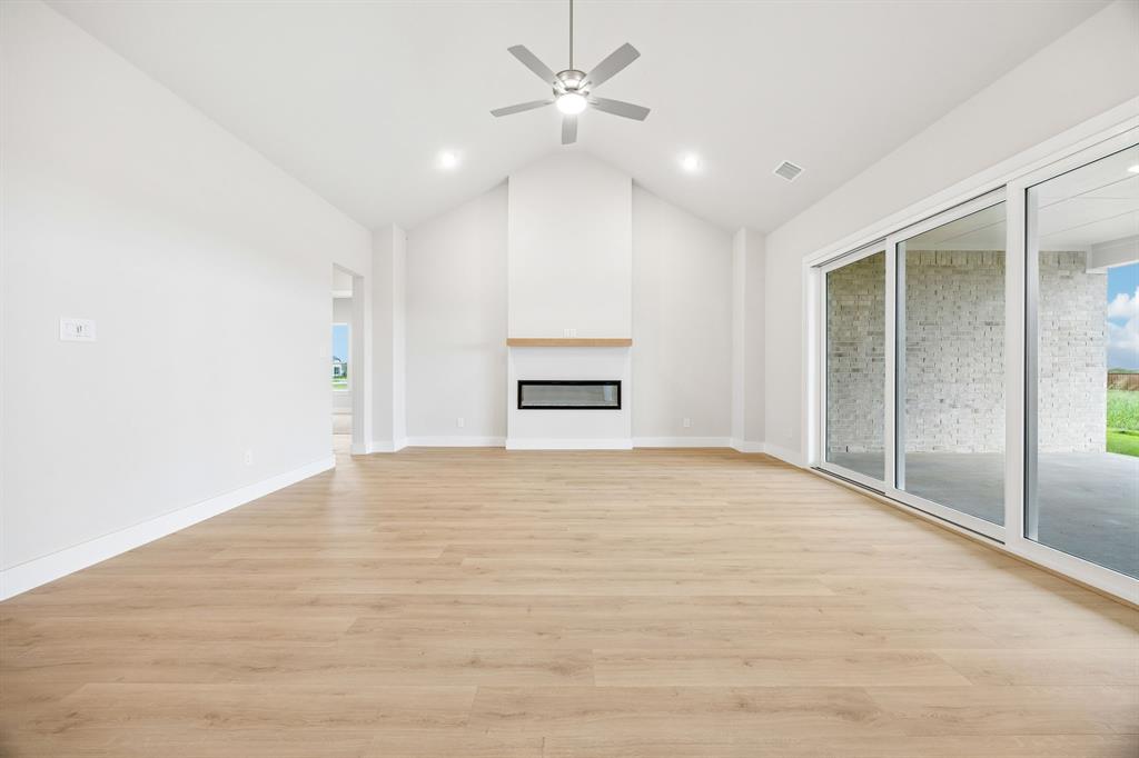 Vaulted ceiling featuring a linear fireplace with wood-finish mantle, wood-finish flooring, recessed lighting, and expansive glass sliding doors