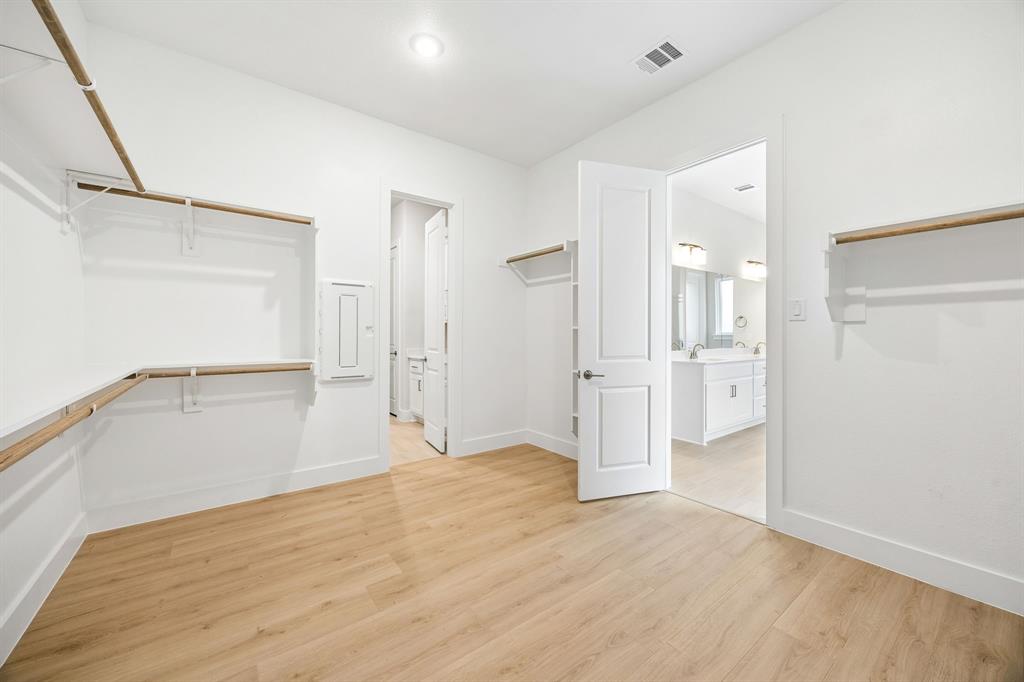 Walk-in storage space featuring wood-finish flooring, multi-tier shelving, recessed lighting, and a six-panel door