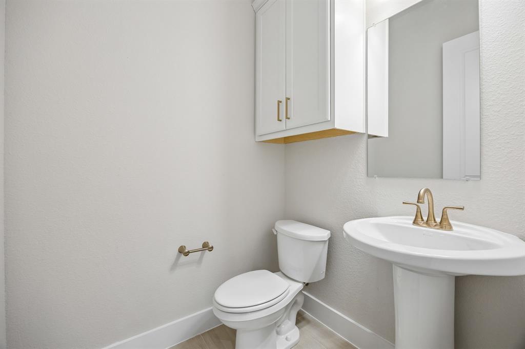 White pedestal sink with a metallic widespread faucet, wall-mounted cabinet with gold-tone hardware, rectangular mirror, and toilet