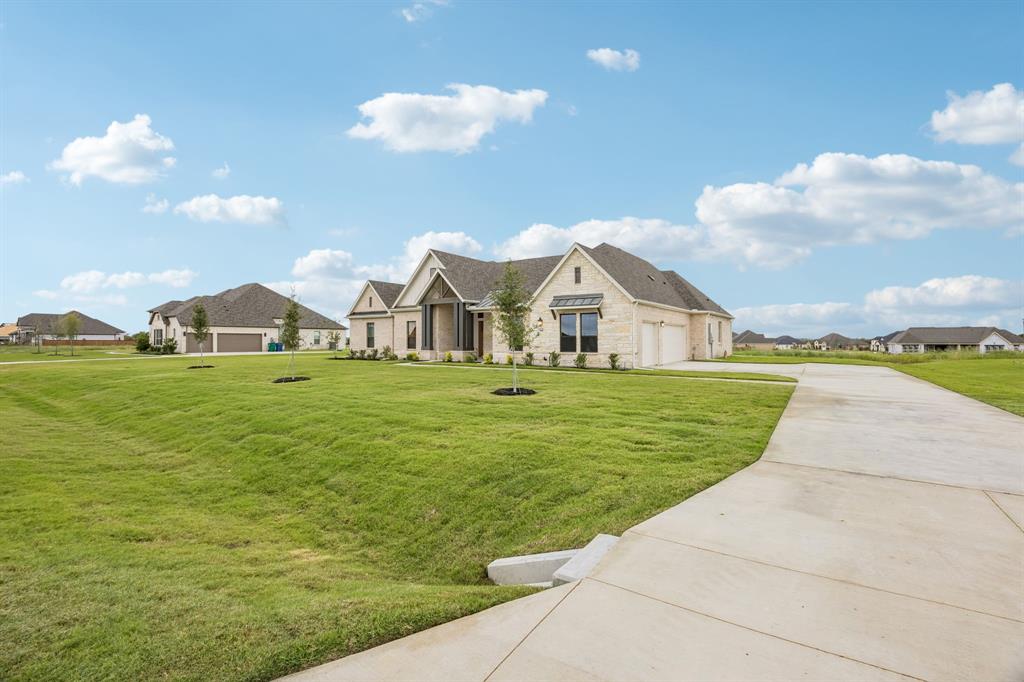 Stone exterior residence featuring a multi-gabled roofline, metal roof accents, an extended concrete driveway, and a spacious front lawn