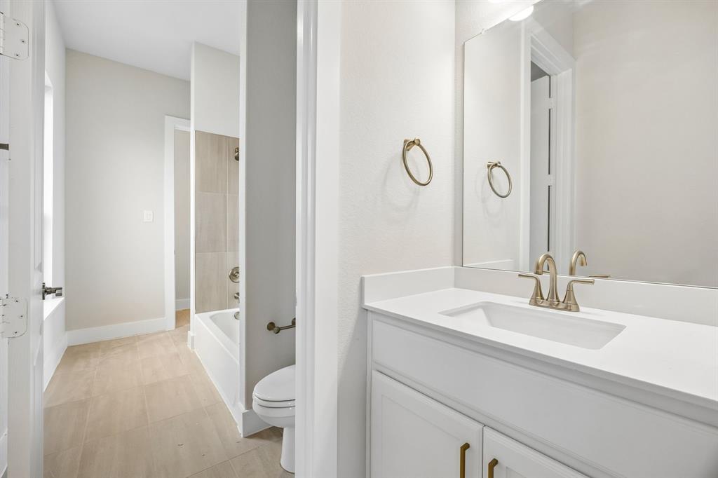 White vanity with solid surface countertop and integrated rectangular sink, brushed metal faucet, full-height wall mirror, and neutral-tone tile flooring extending into the bathing area with tiled tub surround