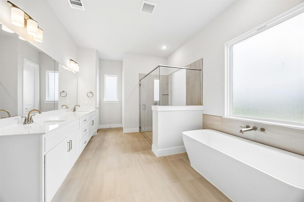 Double vanity with stone-surface countertop, freestanding soaking tub, glass-enclosed shower, and tile-finish flooring