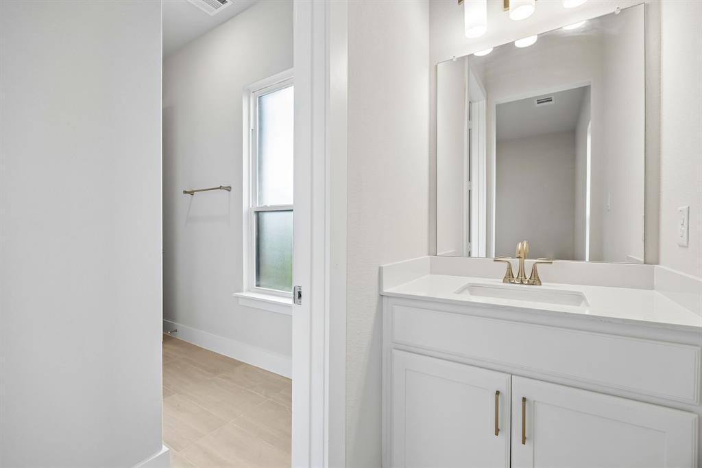 Bathroom featuring a white vanity with a rectangular undermount sink, solid surface countertop, brass-finish faucet, and a wall-mounted mirror with multi-light fixture