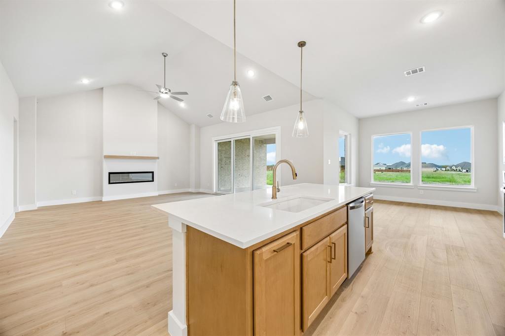Open-concept interior featuring vaulted ceilings, wood-finish flooring, a kitchen island with stone countertops, a linear fireplace, and recessed lighting