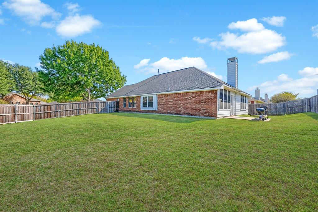 Expansive backyard featuring a brick exterior, shingled roof, exterior chimney, and perimeter wood fencing