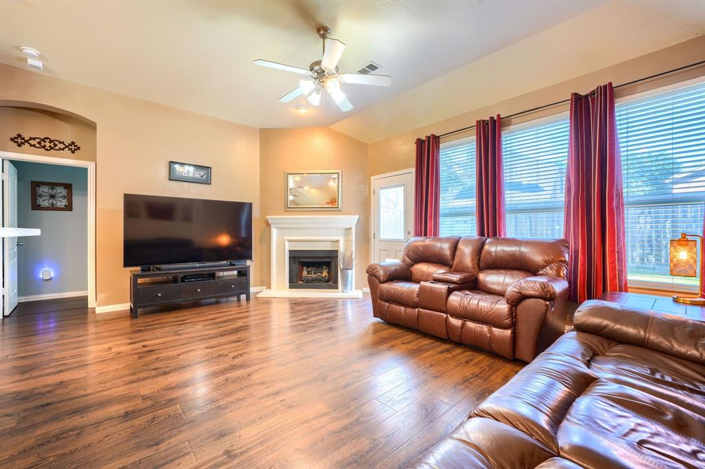 Living area featuring wood-finish flooring, vaulted ceilings, a fireplace with a white mantel, and a multi-blade ceiling fan