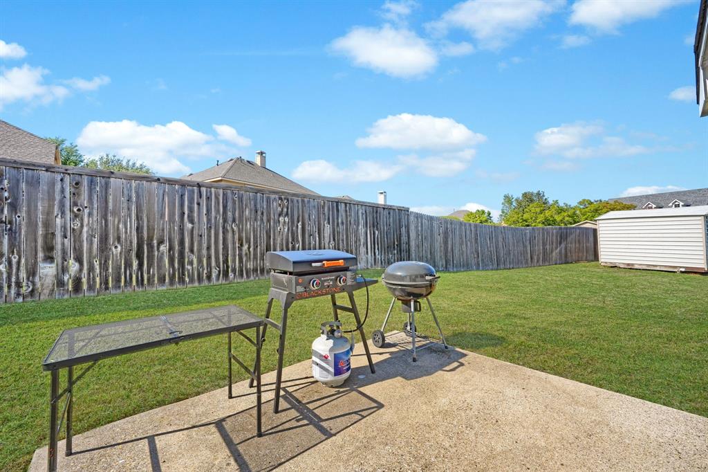 Backyard featuring a concrete patio, wood privacy fencing, a maintained lawn, and a detached storage shed