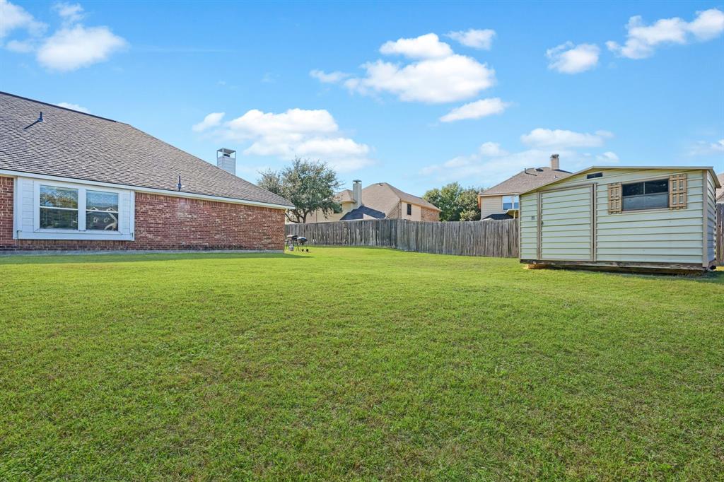 Expansive backyard featuring a brick exterior facade, large lawn, wood fencing, and a detached storage structure