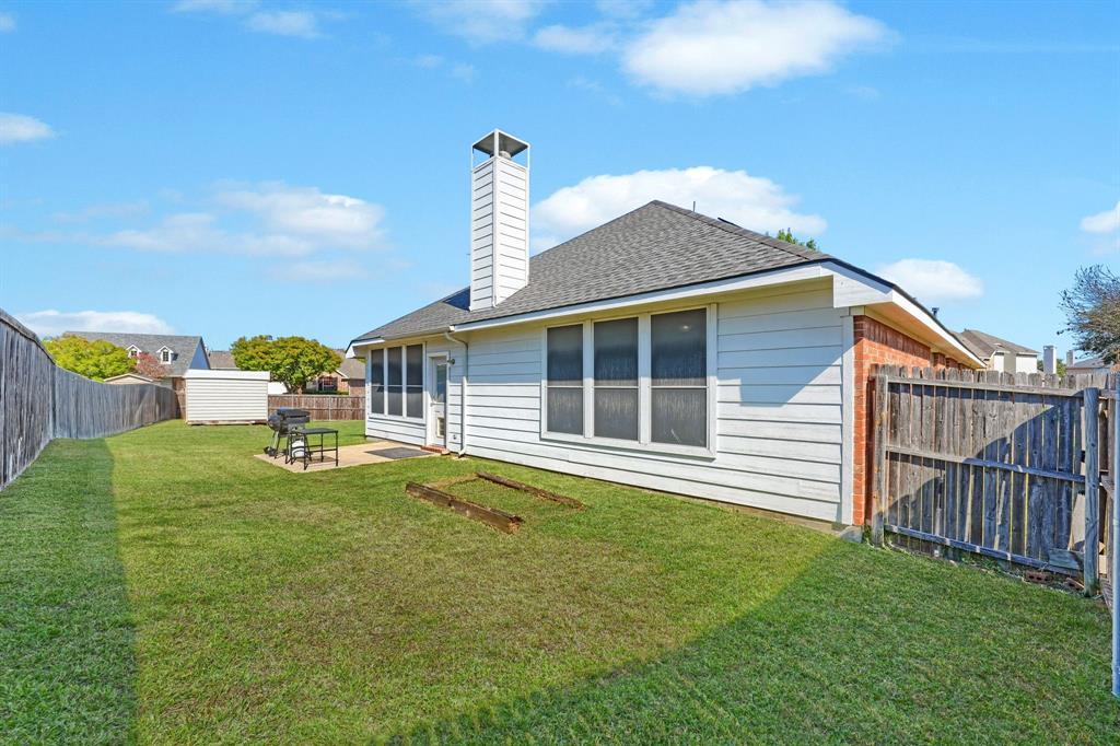 Exterior rear elevation featuring horizontal siding, a central chimney, multiple windows, a concrete patio, and a fenced yard