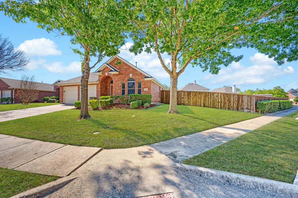 Brick exterior residence featuring an arched entryway, gabled roofline, concrete driveway, and a fenced yard with mature trees Brick exterior residence featuring an arched entryway, gabled roofline, concrete driveway, and a fenced yard with mature trees
