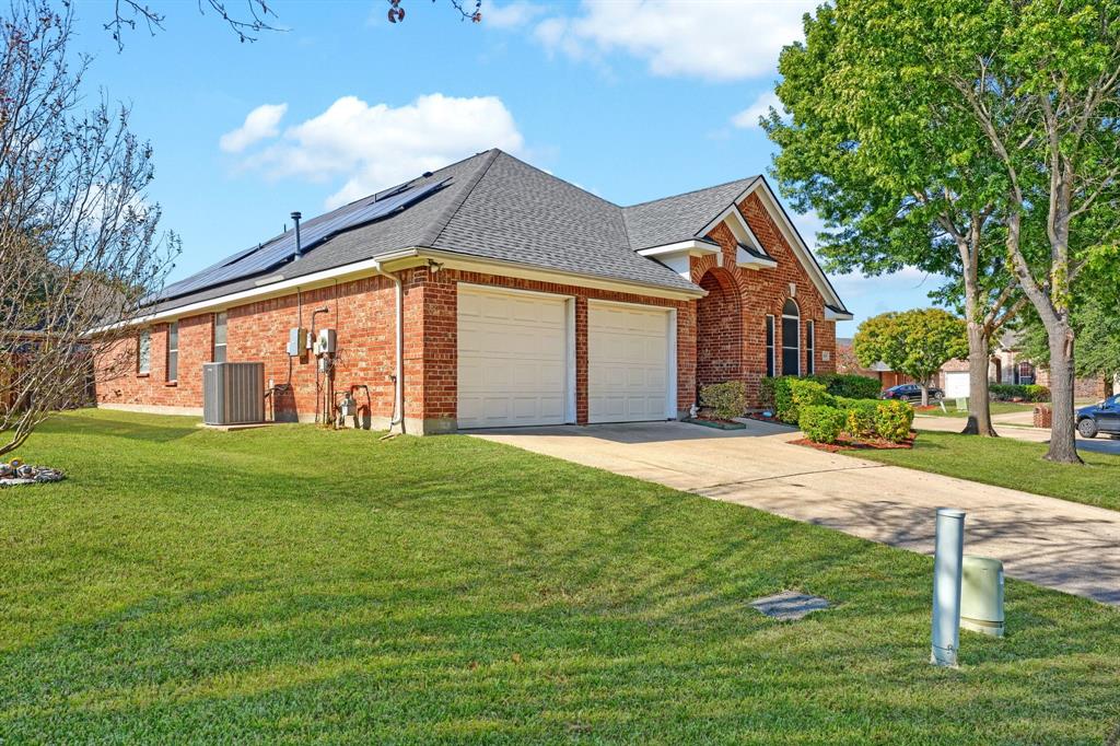 Single-story brick exterior featuring a roof-mounted solar panel array, a two-car garage, and an arched entryway Single-story brick exterior featuring a roof-mounted solar panel array, a two-car garage, and an arched entryway