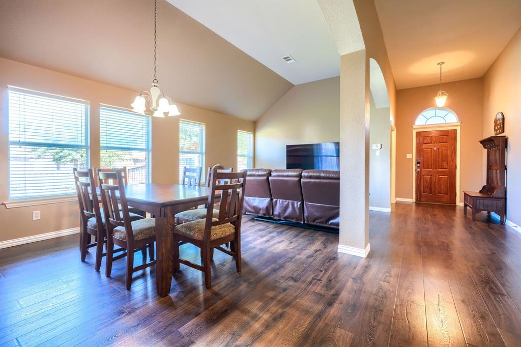 Vaulted ceilings, wood-finish flooring, multi-pane windows with horizontal blinds, decorative pendant lighting, and an arched entryway with a solid wood door featuring a fanlight transom