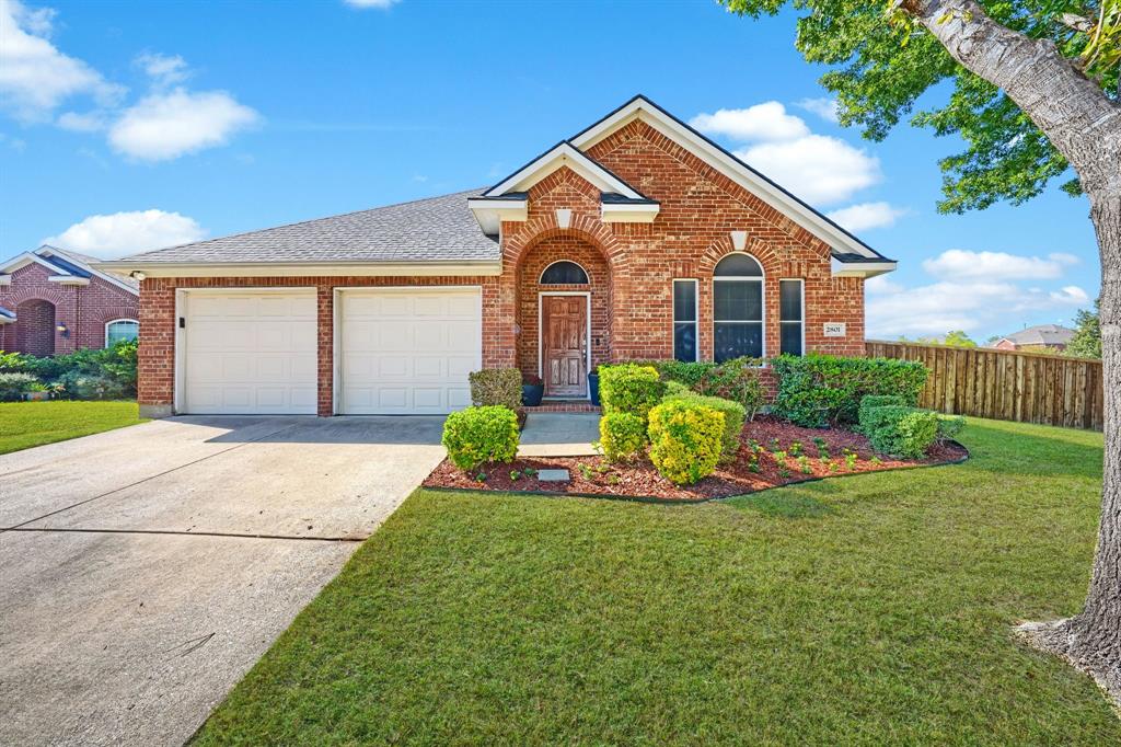 Brick exterior featuring a gabled roofline, an arched entryway, double-car garage, and manicured landscaping
