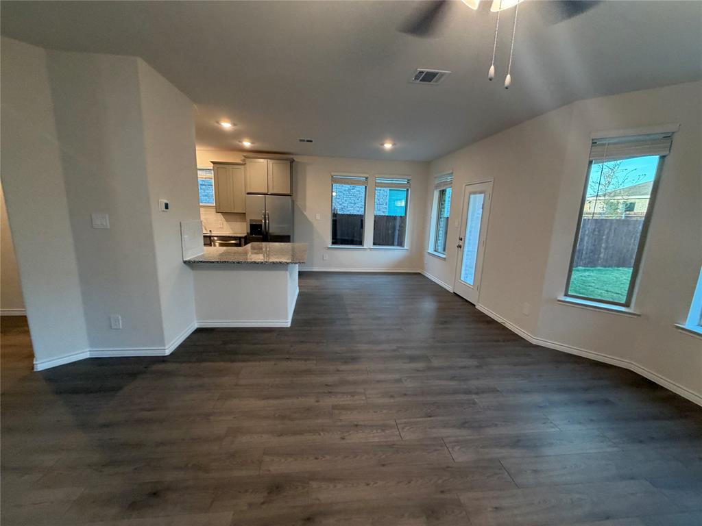Open-concept interior featuring wood-finish flooring, a kitchen peninsula with stone-finish countertops, recessed lighting, and multiple windows