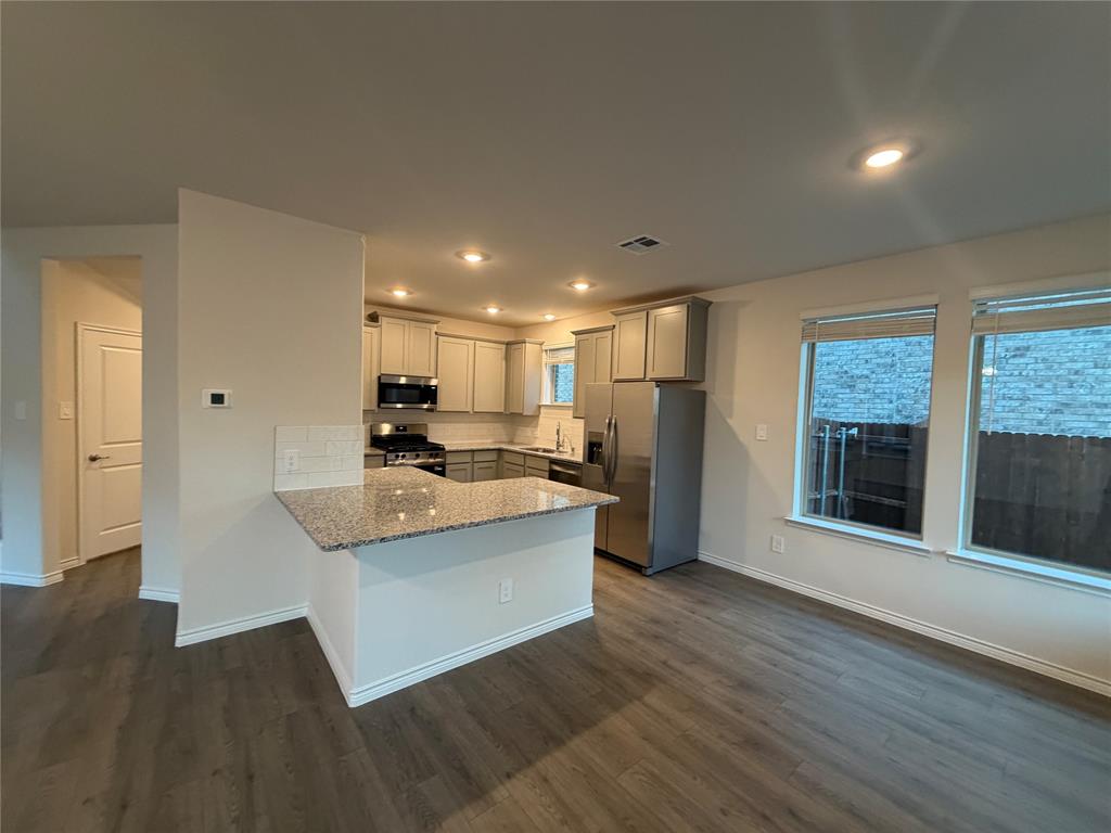 Kitchen featuring wood-finish flooring, stone-surfaced countertops, a breakfast bar, recessed lighting, and stainless steel appliances