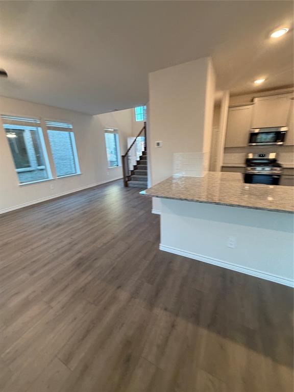 Open-concept kitchen featuring a stone-topped island, wood-finish flooring, recessed lighting, and large windows