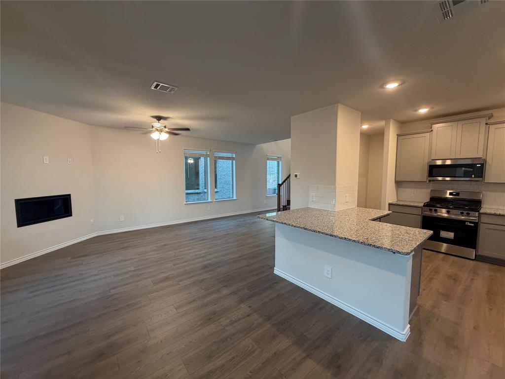 Open concept living area featuring wood-finish flooring, a kitchen island with stone countertops, stainless steel appliances, and a built-in fireplace