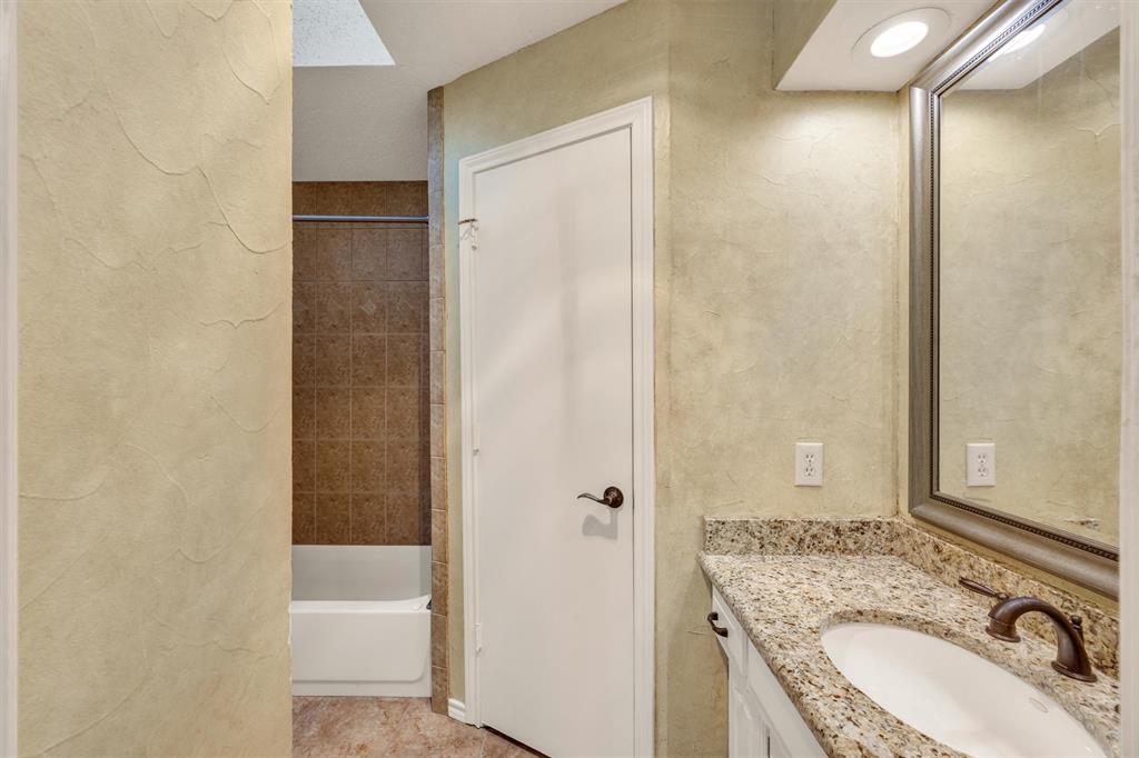 Bathroom featuring a stone-patterned vanity countertop, integrated sink with oil-rubbed bronze fixtures, textured wall finish, and a tub with tiled surround