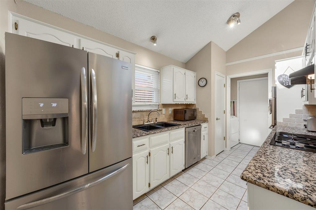 Kitchen featuring vaulted ceilings, stainless steel refrigerator and dishwasher, stone-finish countertops, tile flooring, and white cabinetry