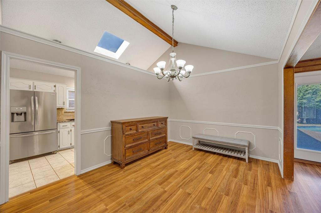Vaulted ceiling with exposed wood beam, skylight, decorative chair rail molding, and multi-arm chandelier
