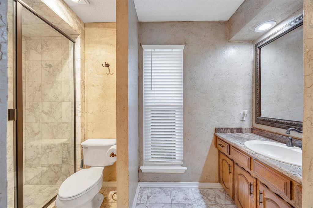 Bathroom featuring a walk-in shower with tiled surround, a vanity with stone-finish countertop, a drop-in sink, and framed wall mirror