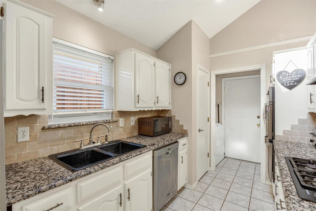 Kitchen featuring white cabinetry, stone-finish countertops, tiled backsplash, double-basin drop-in sink, and stainless steel built-in dishwasher