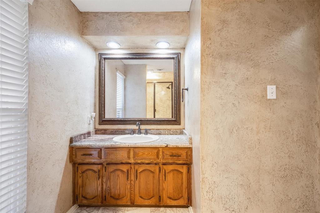 Wood vanity with a natural stone countertop, undermount oval sink, dark metal faucet, and large framed mirror with recessed lighting