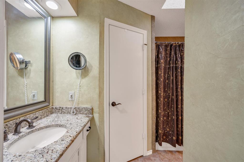 Vanity featuring a stone-composite countertop, undermount oval sink, and metallic faucet hardware, paired with a framed wall-mounted mirror, recessed lighting, and a textured wall finish
