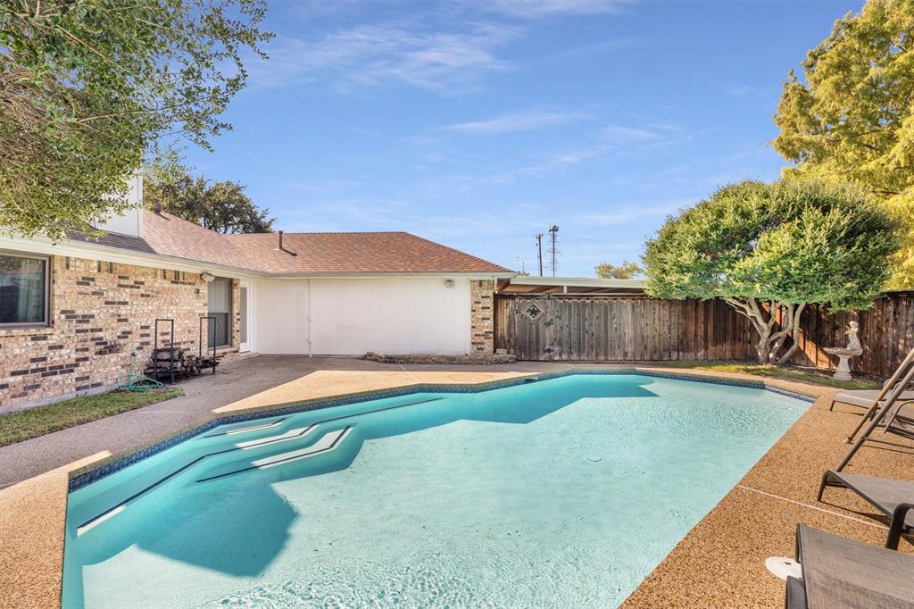 In-ground swimming pool with built-in steps, expansive aggregate concrete patio, brick exterior facade, and wood privacy fencing